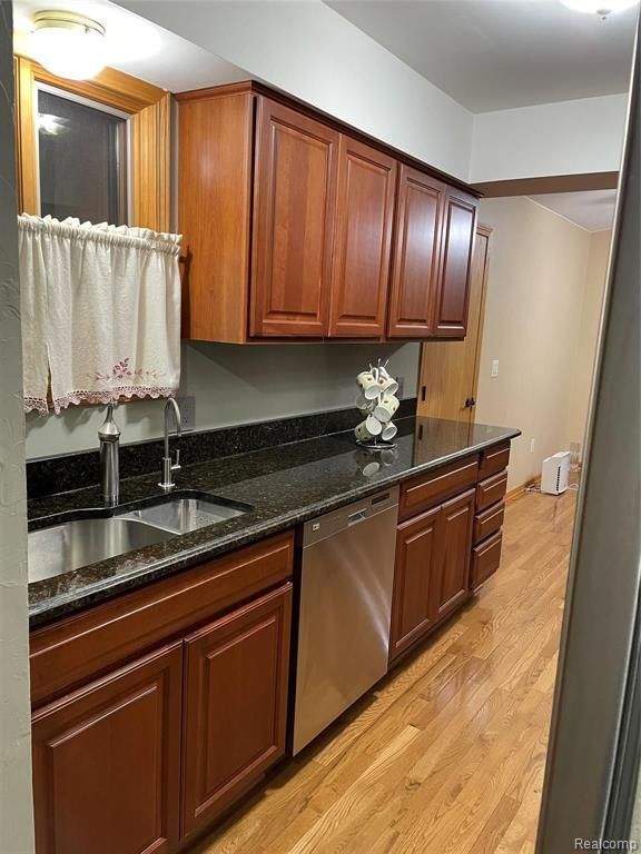 kitchen with dishwasher, light wood-type flooring, dark stone counters, and sink