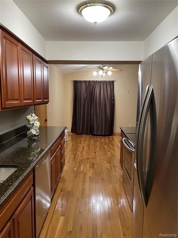 kitchen with ceiling fan, dark stone countertops, light wood-type flooring, and stainless steel appliances