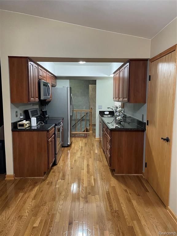 kitchen with dark stone countertops, light wood-type flooring, sink, and appliances with stainless steel finishes