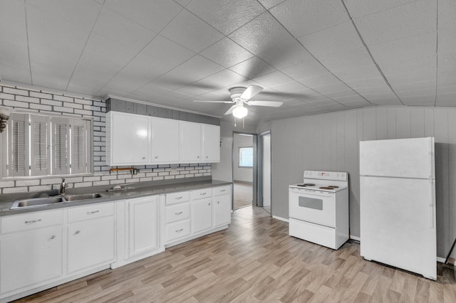 kitchen featuring sink, light hardwood / wood-style floors, white appliances, wooden walls, and white cabinets