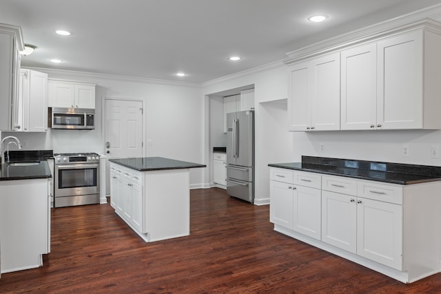 kitchen with appliances with stainless steel finishes, dark hardwood / wood-style flooring, a kitchen island, sink, and white cabinetry