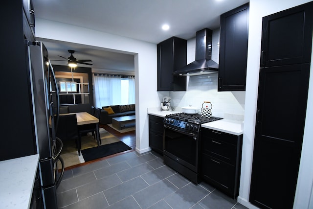 kitchen featuring black gas range, ceiling fan, wall chimney range hood, dark tile patterned floors, and decorative backsplash