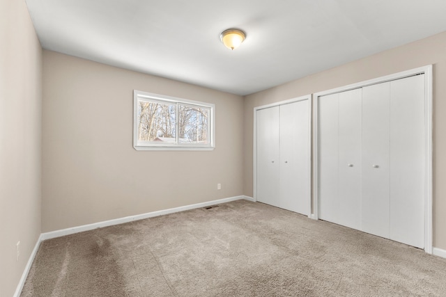 unfurnished bedroom with light colored carpet and multiple closets