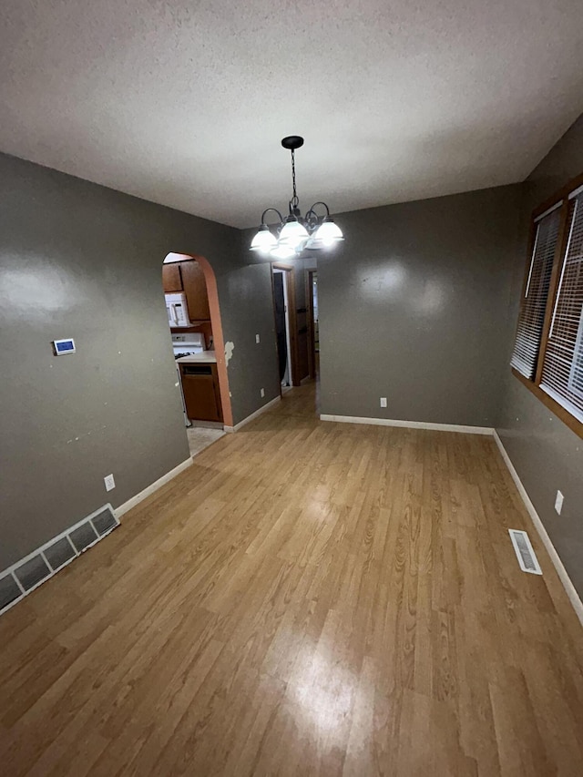 unfurnished dining area featuring a notable chandelier, light wood-type flooring, and a textured ceiling