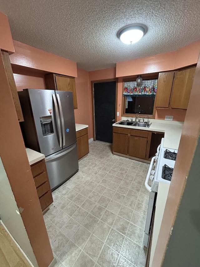 kitchen featuring white stove, sink, stainless steel refrigerator with ice dispenser, and a textured ceiling