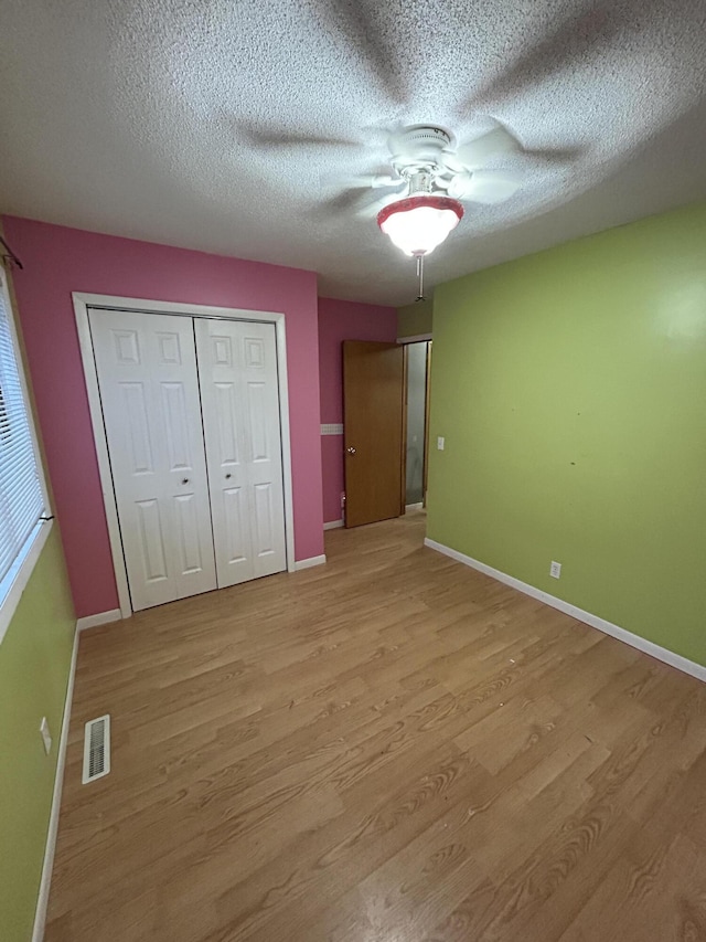 unfurnished bedroom with ceiling fan, a closet, a textured ceiling, and light hardwood / wood-style flooring