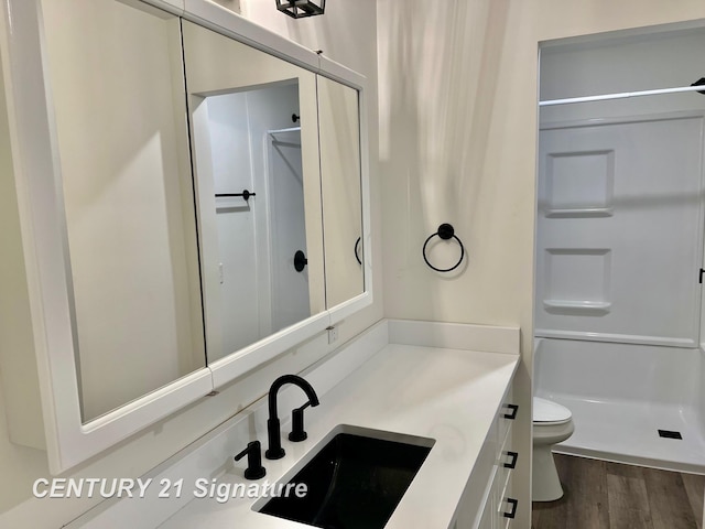 bathroom with hardwood / wood-style flooring, vanity, toilet, and a shower