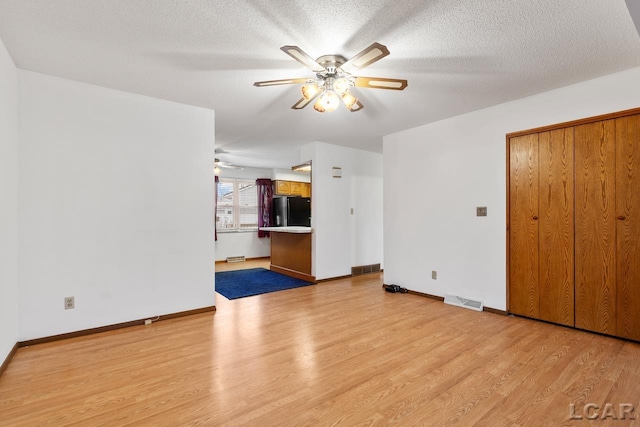 unfurnished living room featuring ceiling fan, light wood-type flooring, and a textured ceiling