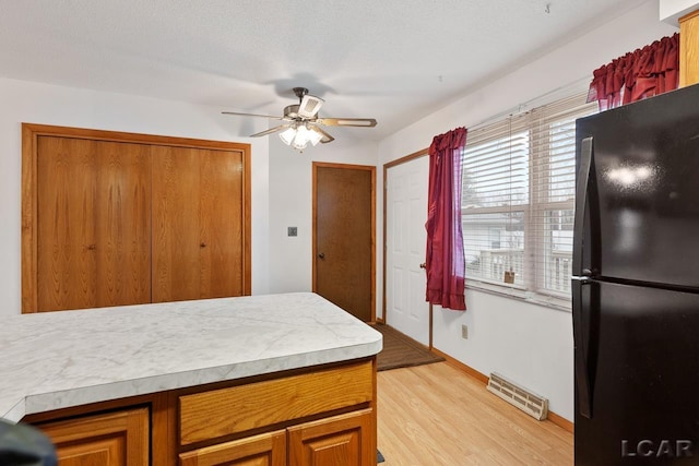 kitchen with a textured ceiling, light hardwood / wood-style floors, black fridge, and ceiling fan