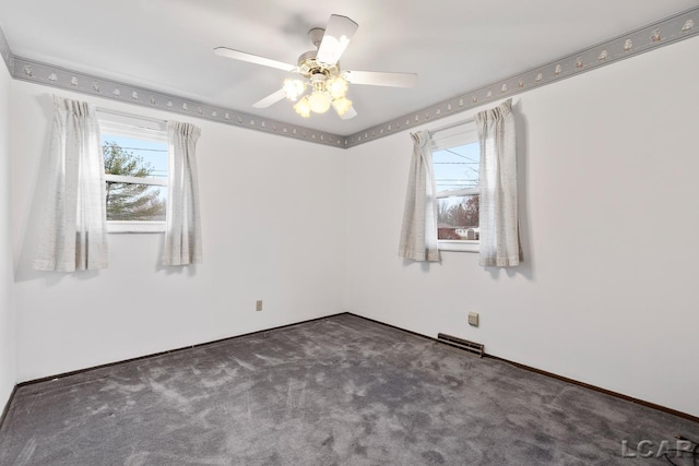 spare room with a wealth of natural light, ceiling fan, and dark colored carpet