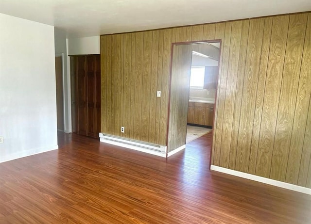 empty room with baseboard heating, wooden walls, and dark wood-type flooring