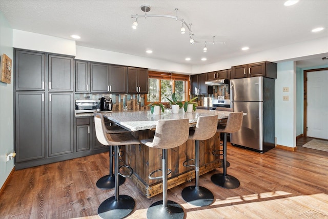 kitchen with a breakfast bar, dark brown cabinetry, a kitchen island, hardwood / wood-style floors, and stainless steel refrigerator