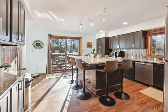 kitchen featuring a breakfast bar area, light hardwood / wood-style flooring, light stone counters, dark brown cabinetry, and stainless steel appliances