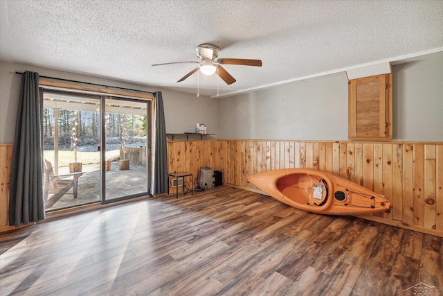 interior space with wooden walls, ceiling fan, wood-type flooring, and a textured ceiling