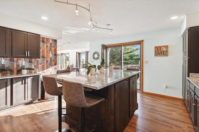 kitchen with a kitchen island, light stone counters, dark brown cabinetry, and a textured ceiling