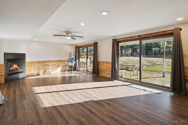 unfurnished living room with a textured ceiling, dark hardwood / wood-style floors, ceiling fan, and a healthy amount of sunlight