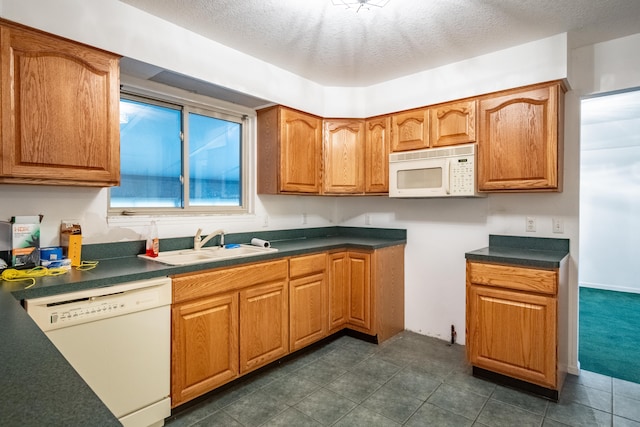 kitchen with a textured ceiling, dark tile patterned floors, white appliances, and sink