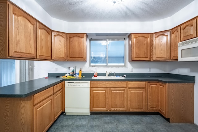 kitchen featuring a textured ceiling, dark tile patterned floors, white appliances, and sink