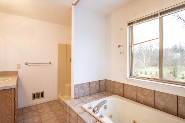 bathroom with a textured ceiling, vanity, a relaxing tiled tub, and tile patterned floors