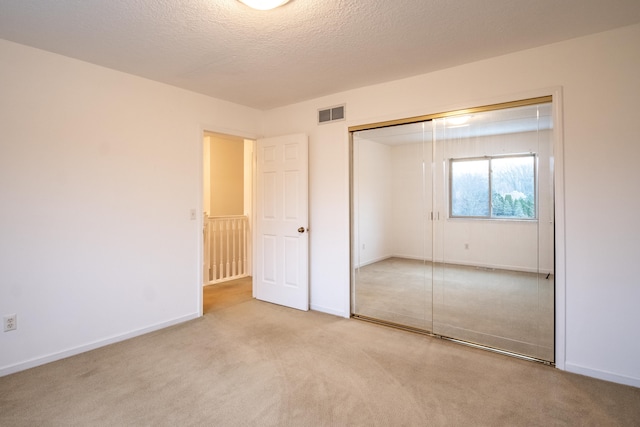 unfurnished bedroom with a closet, light colored carpet, and a textured ceiling