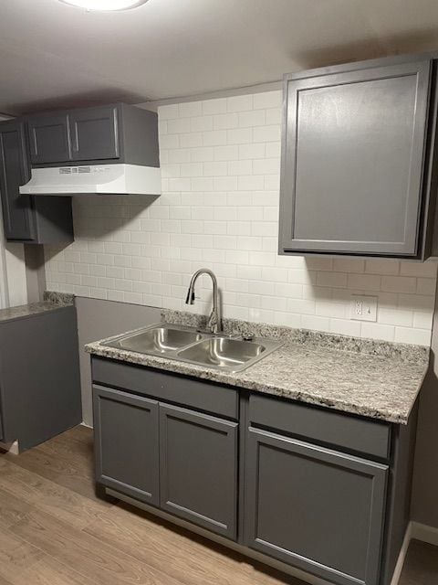 kitchen with backsplash, light hardwood / wood-style floors, gray cabinetry, and sink