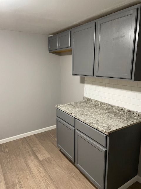 kitchen featuring decorative backsplash, light hardwood / wood-style flooring, gray cabinetry, and light stone counters