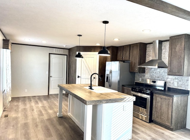 kitchen with a kitchen island with sink, wall chimney exhaust hood, light hardwood / wood-style floors, and appliances with stainless steel finishes