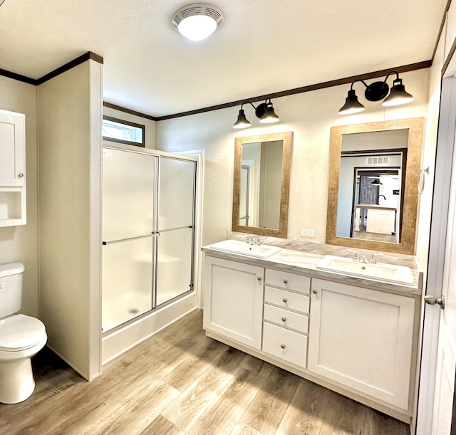 bathroom with wood-type flooring, toilet, vanity, a shower with shower door, and ornamental molding