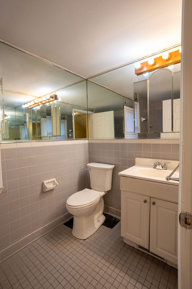 bathroom featuring tile patterned flooring, vanity, toilet, and tile walls