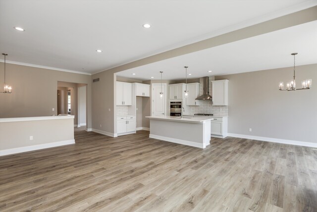 kitchen with wall chimney range hood, decorative light fixtures, decorative backsplash, white cabinets, and light wood-type flooring