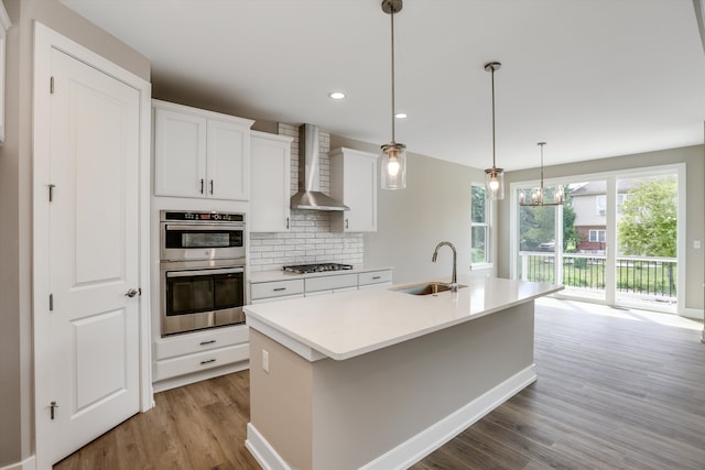 kitchen featuring white cabinets, sink, wall chimney exhaust hood, and an island with sink