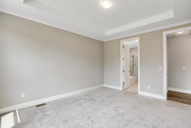 unfurnished bedroom featuring a tray ceiling, ensuite bathroom, and light carpet