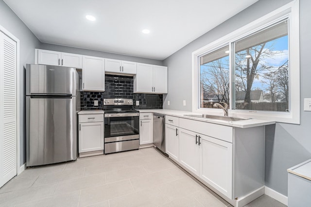 kitchen with appliances with stainless steel finishes, backsplash, sink, light tile patterned floors, and white cabinets