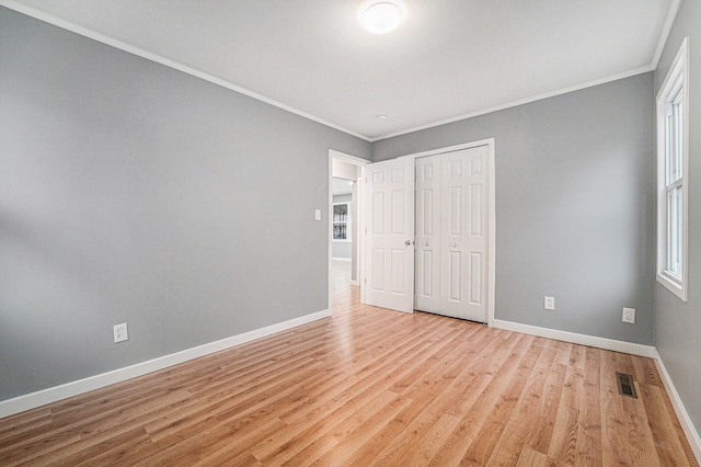 unfurnished bedroom with light hardwood / wood-style floors, crown molding, and a closet