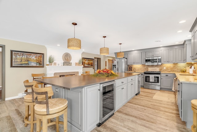 kitchen with gray cabinetry, stainless steel appliances, wine cooler, a kitchen island, and light wood-type flooring