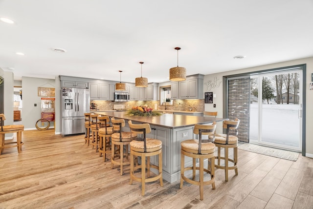 kitchen with a breakfast bar area, decorative backsplash, gray cabinets, light hardwood / wood-style floors, and stainless steel appliances