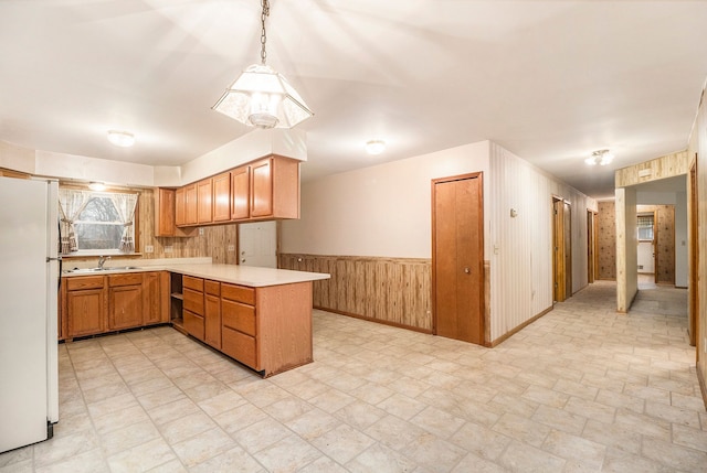 kitchen with kitchen peninsula, sink, decorative light fixtures, white fridge, and wood walls