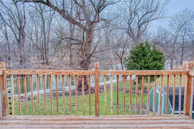 wooden terrace with a yard, a water view, and a storage shed