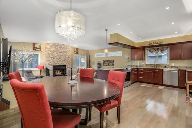 dining space with sink, a chandelier, vaulted ceiling, a fireplace, and light hardwood / wood-style floors