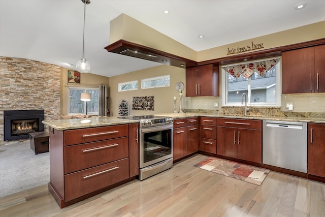 kitchen featuring a stone fireplace, sink, hanging light fixtures, kitchen peninsula, and stainless steel appliances