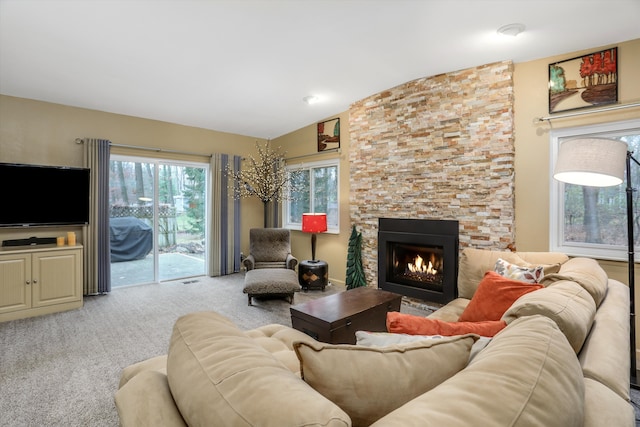 carpeted living room with lofted ceiling and a stone fireplace