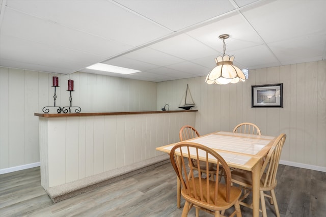 dining space featuring hardwood / wood-style flooring, a paneled ceiling, and wooden walls