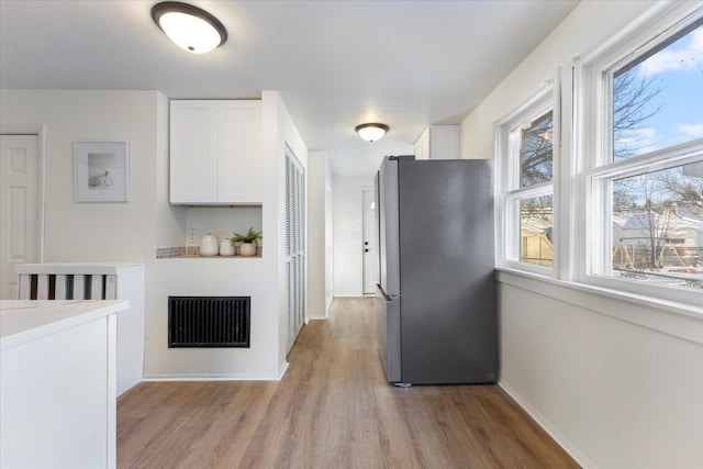 kitchen with stainless steel fridge, light hardwood / wood-style flooring, and white cabinets