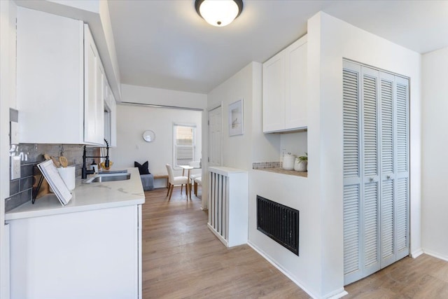 kitchen with backsplash, light hardwood / wood-style flooring, white cabinetry, and sink