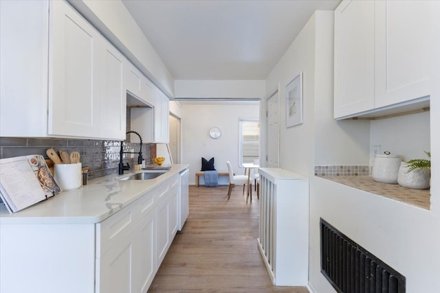 kitchen with backsplash, white cabinetry, sink, and light hardwood / wood-style flooring