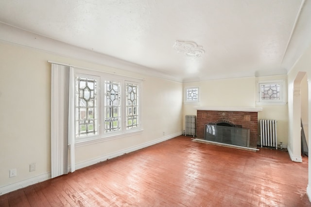 unfurnished living room featuring a brick fireplace, radiator heating unit, and hardwood / wood-style floors