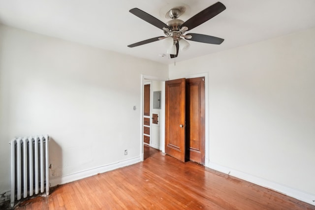 spare room featuring electric panel, ceiling fan, light hardwood / wood-style floors, and radiator heating unit