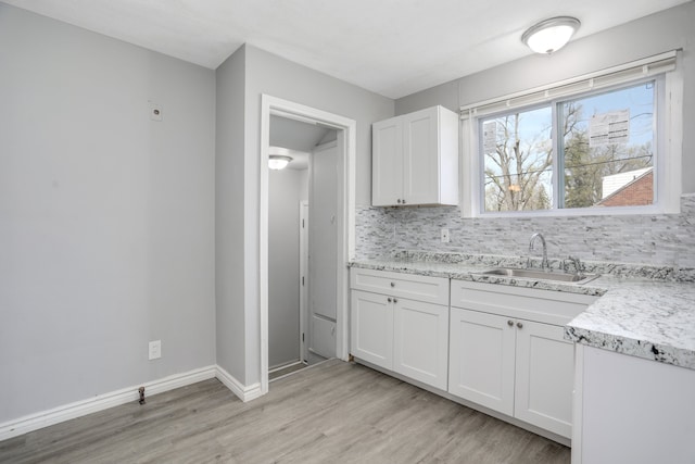 kitchen featuring backsplash, white cabinets, sink, light stone countertops, and light wood-type flooring