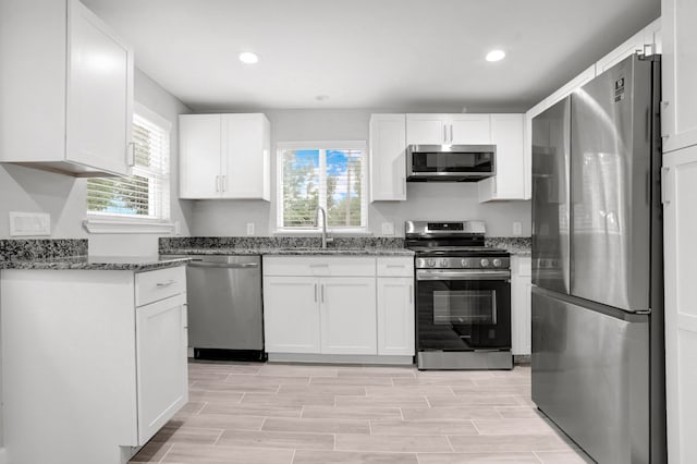 kitchen featuring sink, dark stone countertops, light hardwood / wood-style floors, white cabinets, and appliances with stainless steel finishes