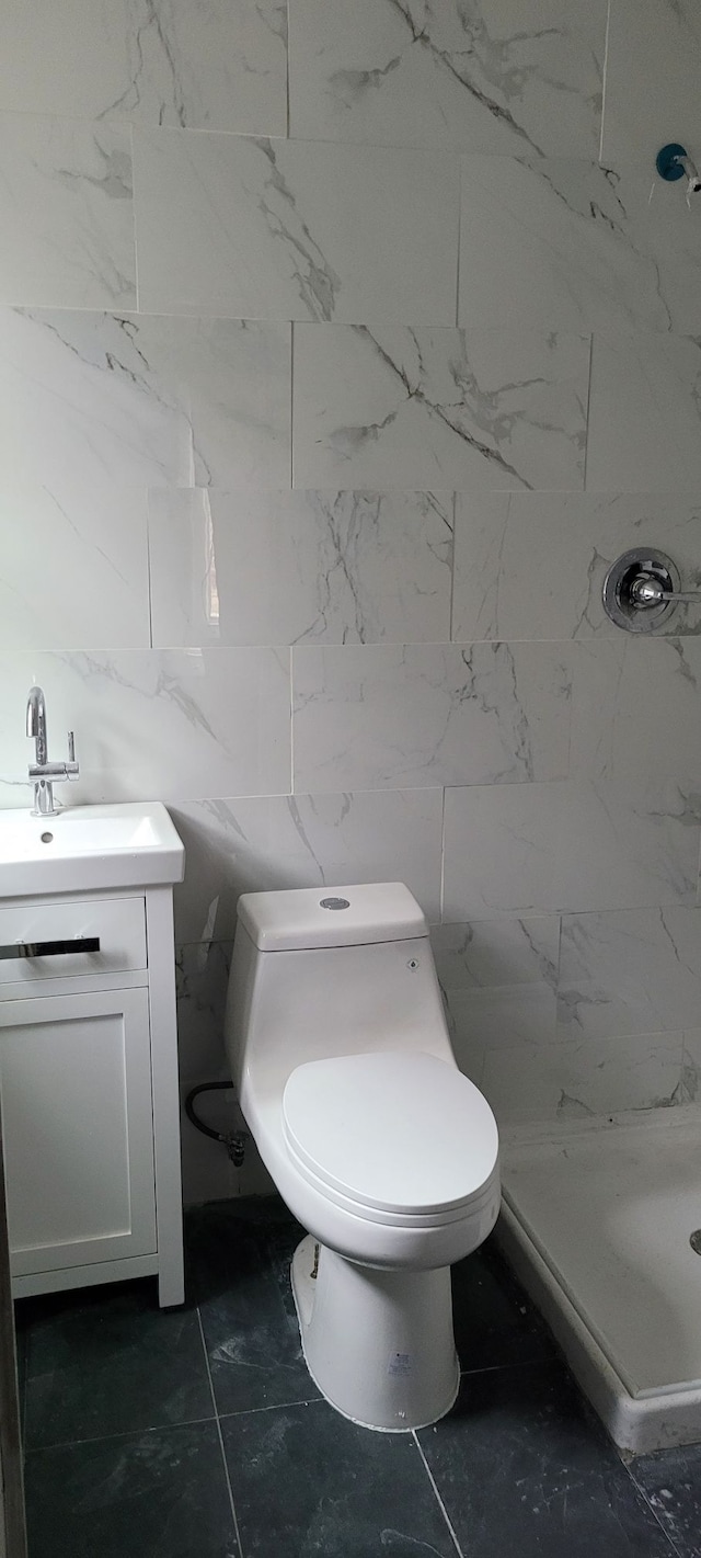 bathroom featuring walk in shower, vanity, toilet, and tile walls